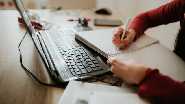 Une femme en train d'écrire sur un carnet devant un ordinateur portable. (Photo d'illustration)