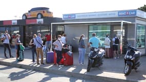 Des vacanciers attendant devant des boutiques de location de voitures à l'aéroport d'Ajaccio en août 2021.