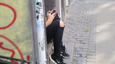Une adolescente assise sur un pas de porte, en train d'écrire sur son smartphone (Photo d'illustration).