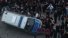 Des hooligans en train de renverser une voiture de police dimanche à Cologne lors d'un rassemblement d'extrême-droite.