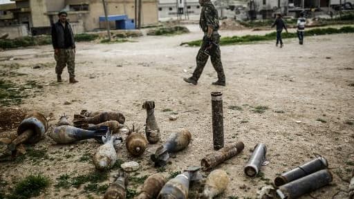 Des combattants kurdes syriens marchent le 27 mars 2015 dans une rue de Kobané au milieu de pièces d'artillerie, deux mois après la reprise de la ville des mains du groupe jihadiste Etat islamique
