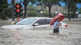 Un homme passe près d'une voiture submergée dans une rue inondée à Zhengzhou en Chine, le 20 juillet 2021