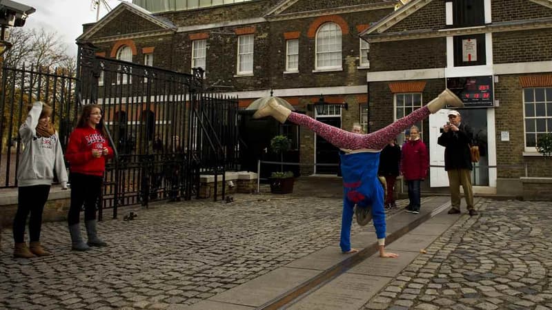 Une jeune fille fait l'équilibre au-dessus de la ligne du méridien de Greenwich à Londres