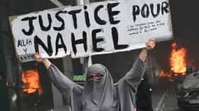 Une participante tient une pancarte "Justice pour Nahel" alors que des voitures brûlent dans la rue à la fin d'une marche blanche pour Nahel, tué par un policier, le 29 juin 2023 à Nanterre