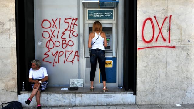 Une femme retirant de l'argent à un distributeur à côté duquel est marqué via un tag "OXI" (Non) (Image d'illustration)