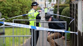 Un officier de police lève un cordon pour permettre à une personne de sortir d'une scène de crime à Hainault, à l'est de Londres, le 30 avril 2024, où un homme de 36 ans brandissant une épée a été arrêté.