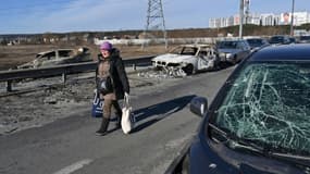Une personne fuyant les combats passe devant des voitures détruites et abandonnées à Irpin, au nord de Kiev, le 12 mars 2022  