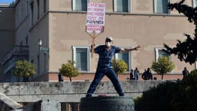 A man holds a placard next to the Greek parliament during a massive demonstration as part of a 24-hour general strike in Athens on November 12, 2015. Around 20,000 people demonstrated against fresh cuts in Athens, with sporadic outbreaks of violence, in the first general strike against the leftist government of Alexis Tspiras who swept to power on an anti-austerity ticket. 
