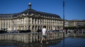 Un passant marche pieds nus sur le Miroir d'eau lors d'une journée ensoleillée à Bordeaux, le 24 juin 2023 en Gironde