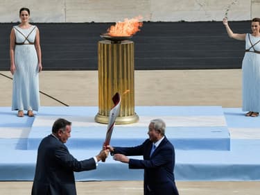 Le vice-président du Comité olympique chinois Yu Zaiqing (à droite) reçoit la torche olympique des mains du patron de l'olympisme grec Spyros Capralos, lors d'une cérémonie à huis clos à Athènes, le 19 octobre 2021