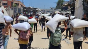 Des Palestiniens portent les sacs de farine qu'ils ont reçus au point de distribution de l'aide distribuée par le Programme alimentaire mondial (PAM) à Khan Yunis, Gaza, le 23 juillet 2025.