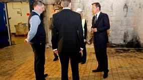 Le Premier ministre britannique David Cameron (à droite), ici dans un supermarché pillé à Salford, dans le nord de l'Angleterre, a recruté un expert américain en sécurité urbaine comme conseiller du gouvernement. /Photo prise le 12 août 2011/REUTERS/Jon S
