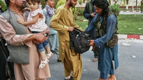 Un taliban (d) fouille les sacs d'Afghans dans une rue de Kaboul, le 16 août 2021