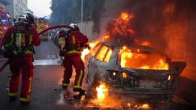 Des pompiers tentent d'éteindre une voiture en feu en marge d'une manifestation à Nanterre,  théâtre d'incidents en soirée, le 27 juin 2023