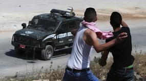 Des Palestiniens lancent des pierres sur un véhicule de police israéliens lors d'affrontements près de Betunia, en Cisjordanie, le 12 juin 2015