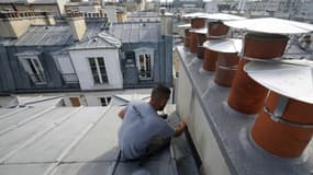 Un couvreur-zingueur répare les solins d'une cheminée pour prévenir les fuites sur le toit d'un immeuble couvert de zinc à Paris, le 31 juillet 2024