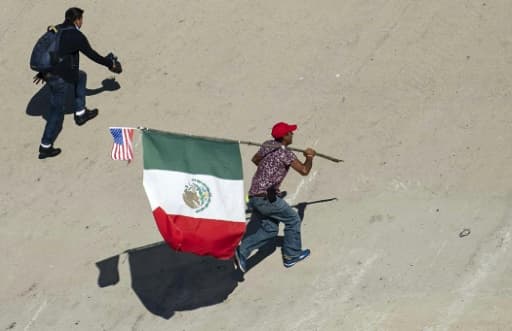 Un migrant portant les drapeaux mexicain et étatsunien tente de passer la frontière entre le Mexique et les Etats-Unis le 25 novembre 2018 à Tijuana Un migrant portant les drapeaux mexicain et étatsunien tente de passer la frontière entre le Mexique et les Etats-Unis le 25 novembre 2018 à Tijuana