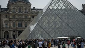 Des touristes font la queue devant la pyramide du Louvre