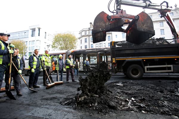 Des ouvriers enlèvent les restes d'un bus incendié d'une route alors qu'un tramway Luas endommagé par le feu se trouve à l'arrière-plan, sur la rue O'Connell à Dublin, le 24 novembre 2023, après une nuit de protestations.