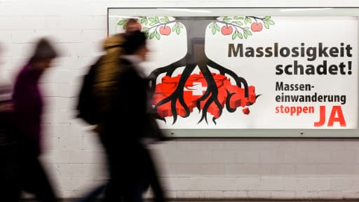 Des passants à Zurich devant une affiche contre "l'immigration de masse" en Suisse.