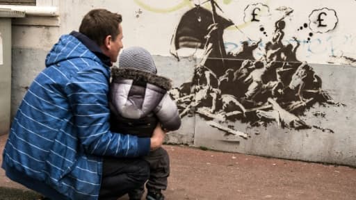 Un homme et un enfant regardent un pastiche de la célèbre toile "Le radeau de la méduse" peint par Bansky sur un mur non loin de la mairie de Calais, le 12 décembre 2015