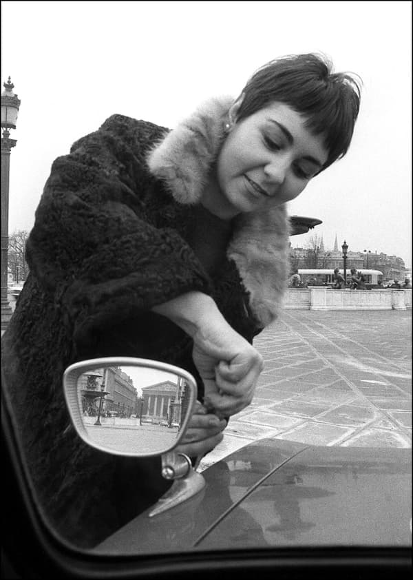 Une jeune femme installe un rétroviseur extérieur sur son véhicule, le 13 mars 1968 à Paris, après la réforme du code de la route qui oblige les automobilistes à équiper leur véhicule de la sorte pour renforcer la sécurité au volant.