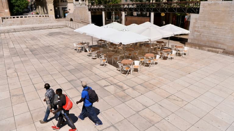 Des passants masqués près d'une terrasse de restaurant désertée à Lérida (Espagne), le 4 juillet 2020