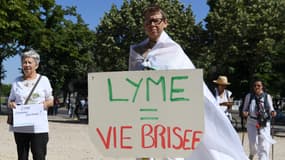 Une femme tient un panneau "Lyme=vie brisée".