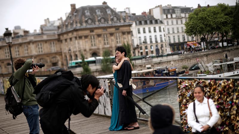 Des touristes se font photographier devant le Pont des Arts. Une partie de la rambarde a déjà été remplacée par du plexiglas.