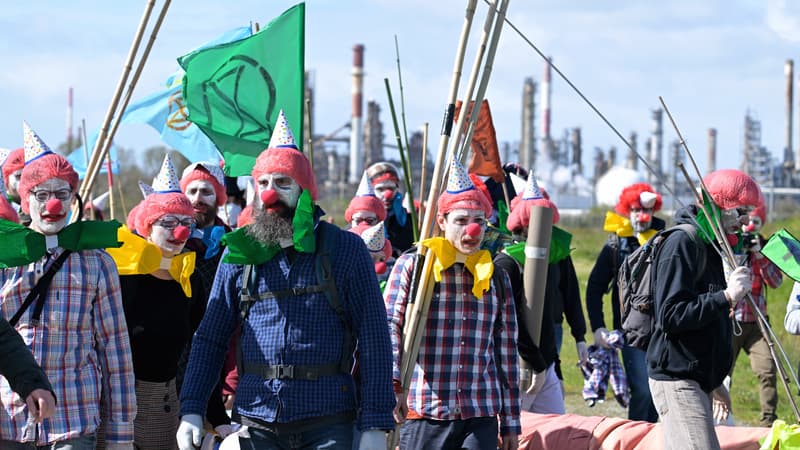 Des militants du mouvement Extinction Rebellion, déguisés en clowns, marchent sur le site de la raffinerie TotalEnergies à Donges (Loire-Atlantique) pour dénoncer l'activité du géant pétrolier français, lors d'une manifestation organisée à l'occasion du 100e anniversaire de l'entreprise, le 23 mars 2024.