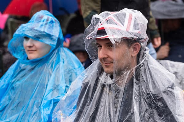 Des spectateurs attendent la procession du roi sous une pluie diluvienne, le 6 mai 2023, à Londres.