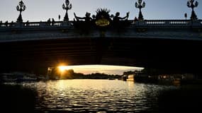 Le soleil apparaît sous le pont Alexandre III au-dessus de la Seine, le 20 août 2023 à Paris
