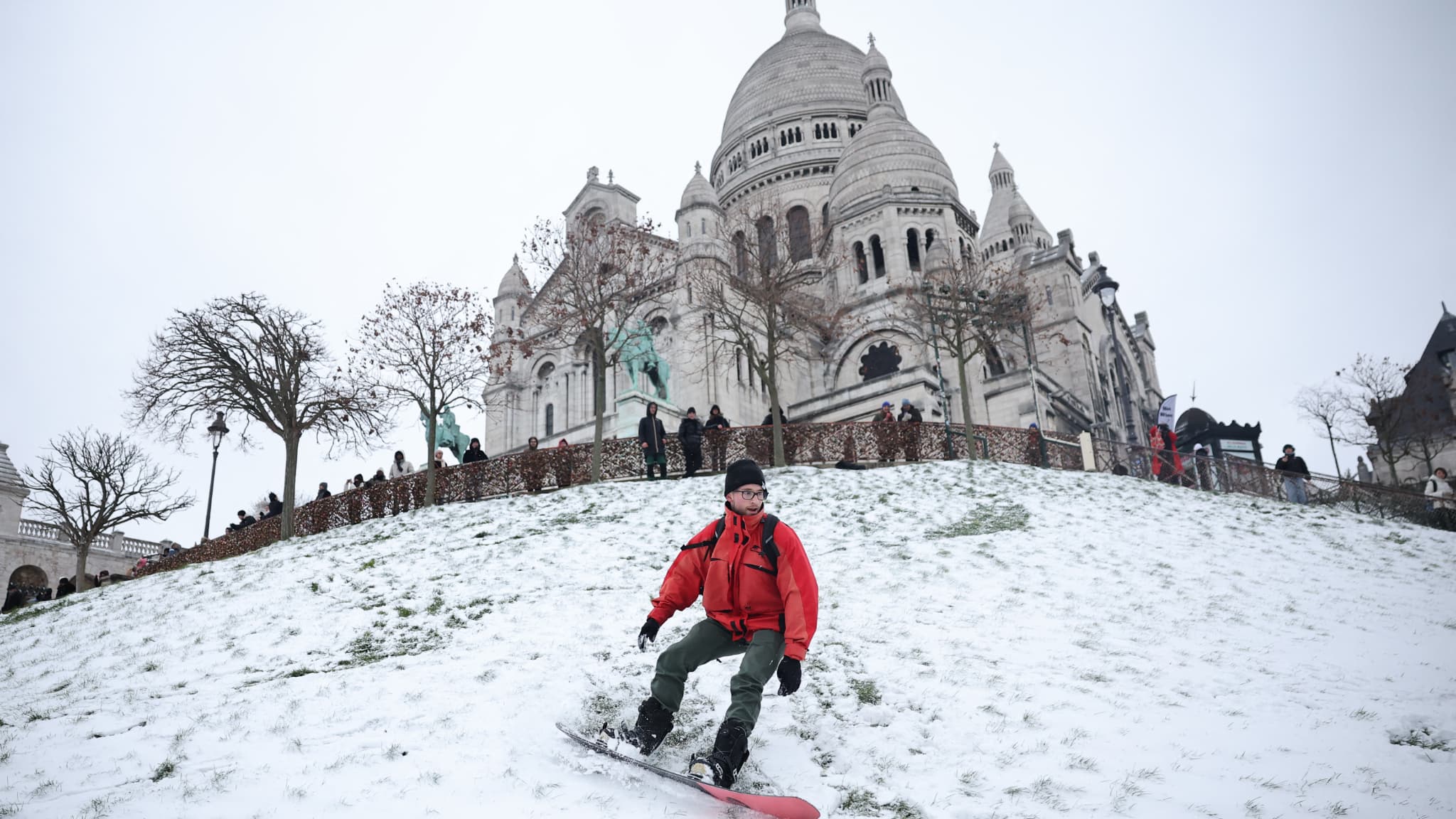 Un snowboardeur dévale une pente enneigée dans le jardin Square Louise Michel, à côté de piétons spectateurs à Montmartre, avec la basilique du Sacré-Cœur en arrière-plan, après les chutes de neige à Paris, le 7 janvier 2026. Un snowboardeur dévale une pente enneigée dans le jardin Square Louise Michel, à côté de piétons spectateurs à Montmartre, avec la basilique du Sacré-Cœur en arrière-plan, après les chutes de neige à Paris, le 7 janvier 2026.