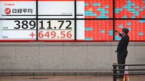 Un homme prend une photo devant un tableau électronique affichant le cours de l'action de la Bourse de Tokyo, dans une rue de Tokyo, le 22 février 2024.