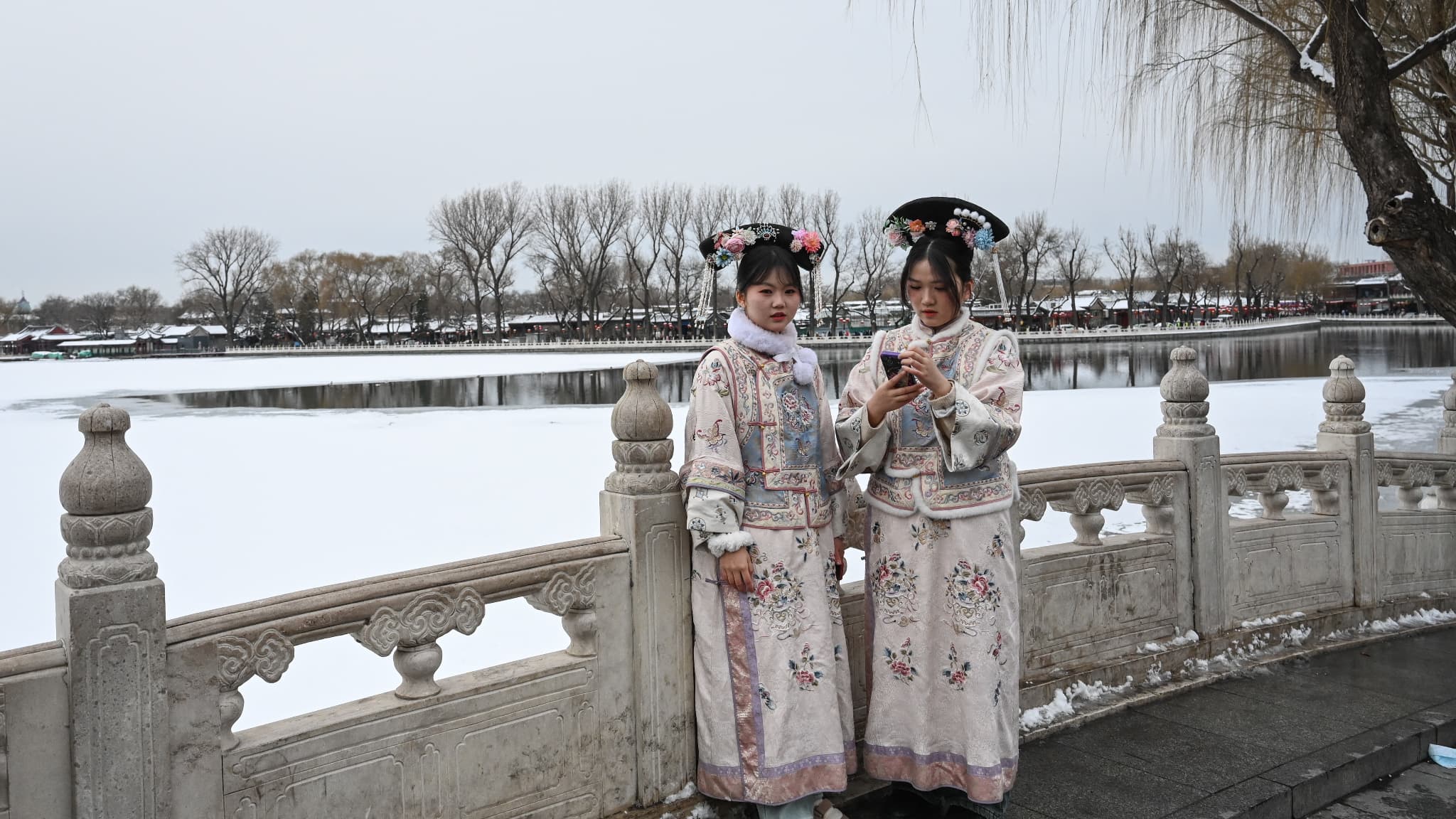 Des personnes vêtues de costumes traditionnels sont vues sur un pont après une chute de neige à Pékin, le 21 février 2024.
