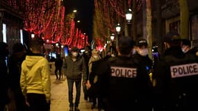 Des badauds passent sur les Champs Elysées à Paris alors que des policiers patrouillent pour faire respecter le port du masque, le 31 décembre 2021