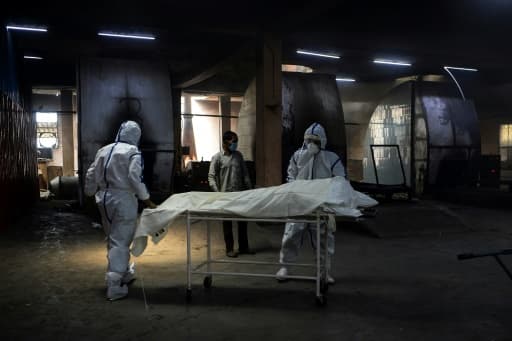 Des employés en combinaison protectrice près d'une civière où repose le corps d'une personne morte du coronavirus avant son incinération, le 3 juin 2020 au crématorium du site de Nigambodh Ghat à New Delhi Des employés en combinaison protectrice près d'une civière où repose le corps d'une personne morte du coronavirus avant son incinération, le 3 juin 2020 au crématorium du site de Nigambodh Ghat à New Delhi