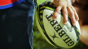 Un ballon de rugby tenu à la main (Illustration).