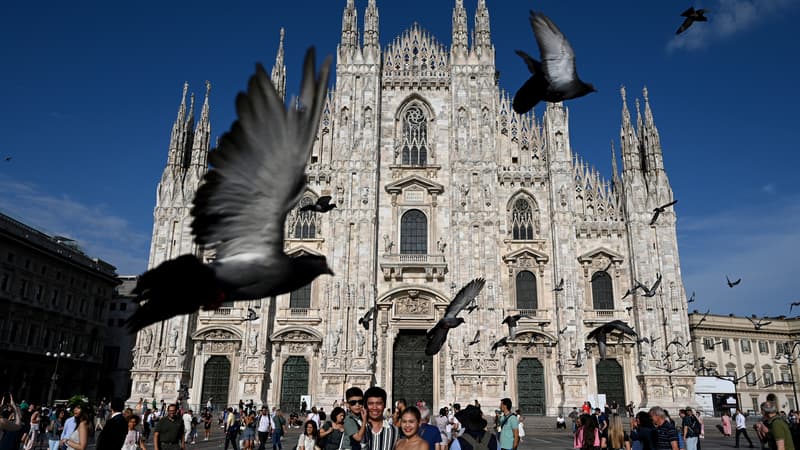 Des touristes posent pour une photo de famille alors que des pigeons passent devant la cathédrale Duomo à Milan, le 6 juillet 2023.