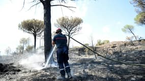 Un pompier continue d'arroser le site d'un incendie pour éviter une reprise de feu, le 20 août 2021 aux Mayons, dans le Var