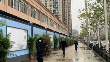 Des habitants portant des masques de protection contre le Covid-19 passent devant le marché aux poissons de Wuhan (centre de la Chine), le 24 novembre 2020