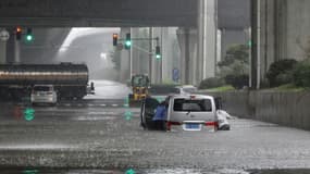 Des habitants de Zhengzhou poussent leur voiture, dans la ville inondée après des orages violents, le 20 juillet 2021