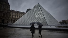 Des touristes s'abritent sous des parapluies devant le musée du Louvre alors que les restes de l'ouragan Kirk provoquent de fortes pluies sur le centre de Paris, le 9 octobre 2024.