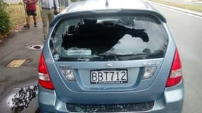 Des passants se tiennent près d'une voiture aux vitres brisées près de la mosquée où s'est produit une fusillade, le 15 mars à Christchurch