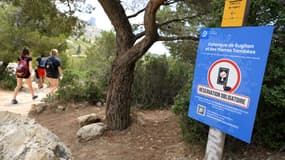 Des randonneurs passent devant un panneau indiquant "réservation obligatoire" sur le chemin de la calanque de Sugiton dans le Parc national des calanques à Marseille, dans le Sud de la France, le 24 juin 2022.