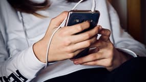 Une jeune femme en train d'écouter ou de regarder du contenu sur son smartphone (Photo d'illustration).