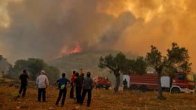 Des personnes se tiennent devant un feu de forêt à Néa Péramos, près d'Athènes, le 19 juillet 2023.