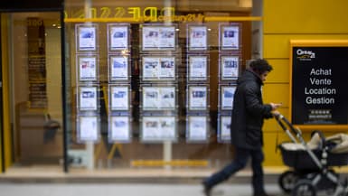 Un homme pousse une poussette en passant devant la vitrine d'une agence immobilière où sont affichées des annonces de vente d'appartements, à Paris. 