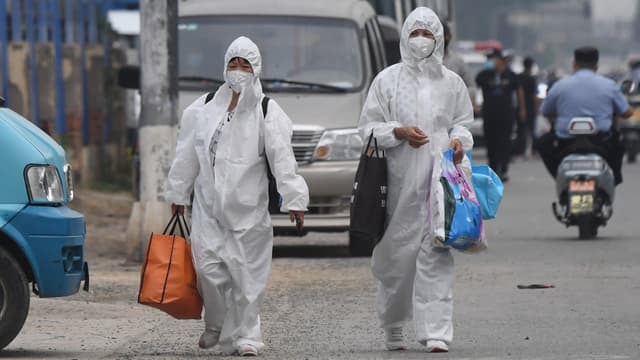 Habitantes vêtues de combinaison de protection à proximité du marché Xinfadi à Pékin, le 13 juin 2020
