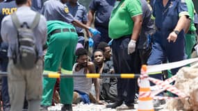 Des mineurs illégaux secourus d'une mine d'or abandonnée sont assis sur le sol tandis que les sauveteurs et les agents du service de police sud-africain (SAPS) enregistrent leurs coordonnées et fournissent une assistance à Stilfontein le 14 janvier 2025. 
